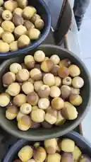This close-up shot provides a detailed view of fresh lotus seeds, also known as 'lotus nuts' or 'heavenly pearls,' displayed in multiple black bowls. The seeds exhibit their characteristic round shape, pale yellow color, and brownish tips. The setting appears to be a market stall or a traditional food shop, suggesting a focus on natural, healthy ingredients. This visual exploration highlights the unique texture and appearance of these nutritious seeds. by @qvalleys with Original Sound by qvalleys