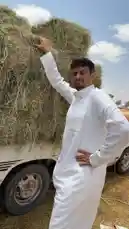 في هذا المشهد، يقف مناحي الرجباني بجانب شاحنة محملة بالقش الجاف تحت سماء صافية ومشمسة. يرتدي ثوبًا أبيض تقليديًا ويبدو أنه يشرح أو يعرض عملية الحصاد، حيث يشير إلى كومة القش الكبيرة ويتحدث مباشرة إلى الكاميرا. تُظهر اللقطات المحيطة بيئة زراعية جافة مع أرضية مغطاة بالقش، مما يوحي بأن الفيديو يوثق نشاطًا زراعيًا يوميًا، مثل جمع القش بعد الحصاد أو إعداده للتخزين. by @manahi.20 with manahi.20 by Original Sound