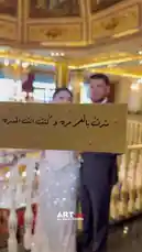 A couple poses for a romantic photoshoot in a stunningly ornate hall. The bride wears a beautiful off-the-shoulder gown while the groom is in a sharp suit. They stand close together, smiling and holding hands, surrounded by golden chandeliers and intricate ceiling artwork. by @artvideo.me with artvideo.me by Original Sound