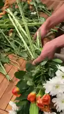 Watch as a skilled florist demonstrates how to create stunning floral arrangements for a long wooden table. This behind-the-scenes look captures the process of preparing fresh flowers like gerberas, lilies, and roses, along with lush greenery, to build a beautiful centerpiece. The final result is a vibrant display of orange, white, and green hues, accented with decorative hats and candles, perfect for a garden party or special event. by @gift_arts1 with gift_arts1 by Original Sound