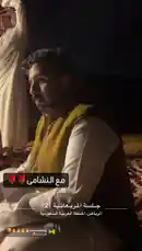 This nighttime scene captures a group of men in traditional Saudi attire socializing outdoors. They are seated on patterned rugs around a low table laden with tea pots and glasses, creating a warm and communal atmosphere. A vehicle is visible in the background, suggesting a casual gathering or a night out. by @tr3i5 with ونعممممممم🔥🔥🔥🔥😍. by فال السعددد😍.