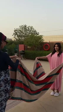 This video shows RJ and a friend setting up a striped blanket by a swimming pool. They arrange a bowl of fresh fruit, sunscreen bottles, and drinks. The scene captures them relaxing together, with one person taking a photo of the setup with a smartphone, creating a casual and fun outdoor moment. by @rjrobes with Original Sound by rjrobes