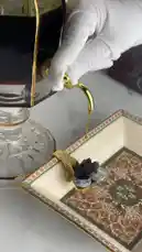 This elegant video showcases a collection of high-end perfumes and oud incense. A hand places a piece of smoldering oud into an ornate tray, releasing fragrant smoke. The scene is set with luxurious glass decanters, a wooden storage box filled with oud chips, and small bottles of perfume, all arranged on a pristine white surface. by @bee.8907 with Original Sound by bee.8907