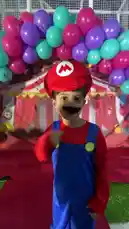 Two adorable children dressed as Super Mario and Luigi strike poses and have fun in front of a festive circus-themed backdrop. The boy playing Mario proudly declares 'It's me, Mario!' while his friend, as Luigi, says 'It's Luigi time!' The scene is filled with colorful balloons and playful energy. by @gioco_23 with Original Sound by gioco_23
