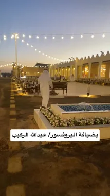 A serene evening at a traditional Saudi venue, where men in white thobes and ghutras stand in formation. String lights illuminate the courtyard as a group chants together in unison, creating a peaceful and culturally rich atmosphere. by @y_alkhmsan with Original Sound by y_alkhmsan