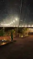 Experience a tranquil journey through a rainy night, starting under a cozy umbrella in a beautifully lit garden filled with vibrant flowers and string lights. The scene transitions to a breathtaking view of a powerful waterfall cascading over rocks, capturing the raw beauty of nature. Finally, the perspective shifts to the inside of a car, where the driver's reflection can be seen in the rearview mirror, suggesting a personal and intimate travel experience. by @karim.alsaleh with حايل القباايل ♥️ by lbi