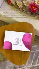 This video features a close-up unboxing of a SOINS perfume set. It begins with the product box on a wooden table, then opens to reveal a 50ml Eau de Parfum bottle and a 35ml 'Pheromone Touch' spray. A hand picks up the bottles, showcasing them to the camera. Arabic text overlays provide information about the brand and its mission. by @soins_sa with Original Sound by soins_sa