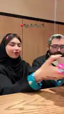 A couple celebrates a special occasion, sharing a delicious-looking chocolate cake. The woman, wearing a black hijab, and the man, in a black shirt, smile and enjoy the dessert together. A text overlay in Arabic reads 'Happy Birthday,' confirming it's a birthday celebration. They take turns feeding each other bites, capturing a sweet and intimate moment. by @soja_design with Original Sound by soja_design