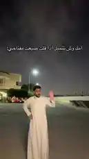In this nighttime scene, Yusuf Abdulrahman demonstrates his style with a crisp white thobe. He stands confidently under a streetlight, adjusting his garment and posing for the camera. Arabic text overlays the scene, inviting viewers to 'Try this look, it suits you perfectly.' This stylish moment captures modern men's fashion in a Middle Eastern context. by @alysf90 with Original Sound by alysf90