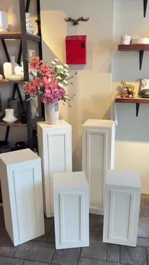 This elegant video showcases a curated display of white pedestal stands arranged in a modern interior setting. The camera pans across the room, highlighting various floral arrangements placed atop the pedestals, including bouquets of pink and orange roses, vibrant mixed flowers in glass vases, and a unique arrangement in a woven basket. Close-up shots reveal the intricate details of the flowers and the clean, minimalist design of the pedestals. The background features shelves with decorative items like vases and a red mailbox, creating a sophisticated and inviting atmosphere perfect for home decor inspiration. by @gift_arts1 with gift_arts1 by Original Sound