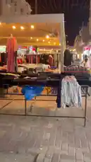 Join us for a vibrant night market tour in Al Jubail, Eastern Province, Saudi Arabia. The camera glides through a bustling outdoor bazaar under a large tent, showcasing a wide array of goods including clothing, accessories, and local crafts. Bright string lights illuminate the scene, creating a lively atmosphere as shoppers browse the stalls. This authentic glimpse into daily life and commerce in Al Jubail offers a rich cultural experience. by @dalilnet with Original Sound by dalilnet