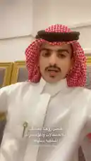 A young man, identified as Khalifa Eid, presents himself in traditional Middle Eastern attire. He wears a white thobe, a red-and-white checkered ghutra secured with a black agal, and sports a neatly groomed mustache and goatee. The setting appears to be an indoor space with ornate, patterned chairs. Throughout the clip, he looks around and speaks, seemingly addressing an audience directly. by @kh-p19 with kh-p19 by Original Sound