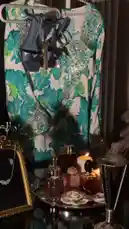 A stylish ensemble is displayed, featuring a vibrant floral dress adorned with sparkling embellishments, paired with elegant dark blue strappy heels. The scene is completed with a curated collection of accessories, including a delicate necklace, perfume bottles, and a lit candle, creating a sophisticated and glamorous atmosphere. by @ab.7955 with Original Sound by ab.7955