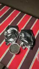 A close-up view shows hands opening foil-wrapped packages on a striped tablecloth. A small cup filled with dark, granular material is presented, suggesting a product review or unboxing of an unknown substance. by @azozi.5562 with Original Sound by azozi.5562