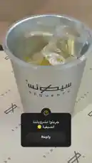 A close-up view shows a clear plastic cup with the 'Sequence' logo being filled with a light-colored liquid over ice. The drink fizzes as it's poured, creating a refreshing beverage. by @sequence-coffee with For a good mood by 🪩✨