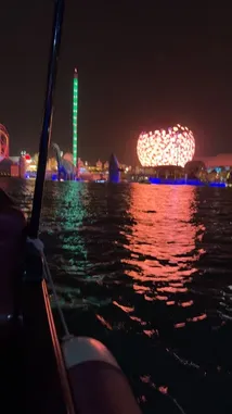 Experience the vibrant night view of Dubai Parks and Resorts from a boat. The camera captures the illuminated skyline, including the iconic Ain Dubai observation wheel and other attractions like the roller coaster and water park, all reflected beautifully on the water. This scenic tour offers a unique perspective of the entertainment destination after dark. by @guruofmarketing with Original Sound by guruofmarketing