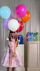 A young girl showcases a variety of colorful mini handbags from the JOY NARCISSUS brand. She models different styles, including pink, blue, black, and purple bags adorned with fun charms and stickers, while wearing a charming floral dress. The setting includes festive balloons and a display cabinet, creating a cheerful and stylish atmosphere perfect for kids' fashion inspiration. by @joy.narcissus with Original Sound by joy.narcissus