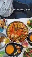 An overhead view captures a massive seafood boil feast, featuring snow crab legs, shrimp, mussels, corn on the cob, and potatoes, all generously seasoned and served in a large metal bowl. The table is set with side dishes like grilled bread, salad, and various colorful cocktails, creating an inviting and delicious dining experience perfect for sharing. by @marvedtv with Original Sound by marvedtv