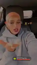 A woman, identified as Nurse Amal, films herself in a car wearing a light gray hoodie and a peach-colored hijab. She poses for the camera, making direct eye contact and using hand gestures. The setting is the interior of a vehicle during the day. On-screen graphics include Arabic text, a bear emoji, and a heart emoji. by @ilwaad67 with وانا وياااااااااااااكً by ❤️❤️❤️❤️❤️❤️❤️❤️❤️❤️