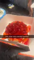 A close-up, high-quality shot of a delicious-looking strawberry cheesecake in a white box. The cake is topped with fresh strawberries and a vibrant red glaze, presented on a dark marble countertop. This enticing visual is designed to capture attention and encourage further exploration. by @marvedtv with Original Sound by marvedtv
