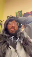 A person wearing a long black wig, glasses, and a grey hoodie films a selfie-style video in their room. They run their hand through their hair while looking at the camera. The text 'Tuesday 9:42 AM' is overlaid on the screen. In the background, a painting and a guitar are visible on the wall. by @ford_fetti with Original Sound by ford_fetti