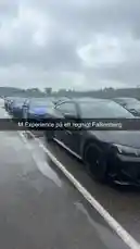 En rörelsefull bild från en regnig dag på Falkenberg där en svart M-bil står i kö med andra sportbilar. Texten 'M Experience på ett regnigt Falkenberg' är tydligt synlig över bilden. Scenen fångar spänningen och atmosfären vid ett tävlings- eller testkörningsarrangemang under dåliga väderförhållanden. by @tershine with original sound