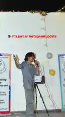 A dynamic individual takes the stage at an event, holding a microphone and phone, seemingly sharing an update. The setting includes banners, balloons, and festive decorations, suggesting a college or youth gathering. Text overlays indicate an 'Instagram update,' blending live performance with social media storytelling. by @lil.ishhhh with Original Sound by lil.ishhhh
