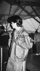 A stylish individual in a leather jacket stands in profile against a geometric architectural backdrop. The scene is captured in a classic black and white film style, creating a timeless urban atmosphere. A poetic quote in Hindi overlays the image, adding a layer of introspection and artistic depth. by @lil.ishhhh with Original Sound by lil.ishhhh