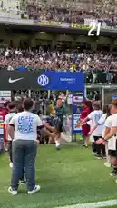 In a vibrant pre-match atmosphere, Inter Milan players stride onto the pitch, shaking hands with young ball kids in a traditional gesture before kickoff. Dressed in their distinctive blue patterned jerseys sponsored by Qatar Airways, the squad moves through a tunnel entrance into the stadium. The stands are filled with fans waving flags and cheering, creating an electric ambiance. This moment captures the anticipation and team spirit just before the start of an Inter Milan game. by @interofficial with Original Sound by interofficial