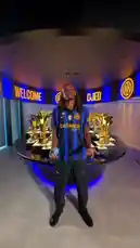 A fan holds a blue Spider-Man figurine inside the FC Internazionale Milano trophy room. An Inter Milan player, wearing the team's blue and black striped jersey, walks into the frame and takes the figurine from the fan. The scene captures a special moment of fan interaction within the club's prestigious display. by @interofficial with Original Sound by Contains: Blitzkrieg Bop - Ramones
