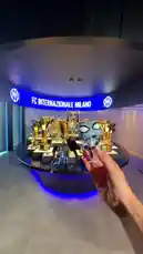 A fan holds a blue Spider-Man figurine inside the FC Internazionale Milano trophy room. An Inter Milan player, wearing the team's blue and black striped jersey, walks into the frame and takes the figurine from the fan. The scene captures a special moment of fan interaction within the club's prestigious display. by @interofficial with Original Sound by Contains: Blitzkrieg Bop - Ramones