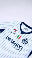 This video provides a detailed showcase of Inter Milan's new away football jersey. It begins with a close-up of the iconic club crest, then pans out to reveal the full design, which features white with thin blue vertical stripes, a navy blue V-neck collar, and navy blue sleeve cuffs. The front displays prominent sponsor logos including 'betsson sport' and the Nike swoosh. The video includes detailed shots of the Italian Serie A patch, the U-Power logo on the sleeve, and the interior neck label which reads 'INTER MILANO', 'AERO-FIT', and 'MADE IN GEORGIA'. This visual presentation highlights the kit's aesthetic and branding elements. by @interofficial with original sound