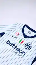This video provides a detailed showcase of Inter Milan's new away football jersey. It begins with a close-up of the iconic club crest, then pans out to reveal the full design, which features white with thin blue vertical stripes, a navy blue V-neck collar, and navy blue sleeve cuffs. The front displays prominent sponsor logos including 'betsson sport' and the Nike swoosh. The video includes detailed shots of the Italian Serie A patch, the U-Power logo on the sleeve, and the interior neck label which reads 'INTER MILANO', 'AERO-FIT', and 'MADE IN GEORGIA'. This visual presentation highlights the kit's aesthetic and branding elements. by @interofficial with original sound
