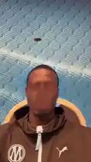 A player from Olympique de Marseille sits in front of a blue textured wall, initially with his face obscured. He then removes the filter, smiles, and speaks directly to the camera while upbeat music plays in the background. by @omofficial with Original Sound by omofficial