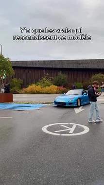 A vibrant blue Mazda RX-7 drifts through a parking lot, showcasing its modified body kit and gold wheels. The car, driven by AnasDC, navigates tight turns as onlookers watch. The scene captures the essence of European car culture. by @anasdc01 with Original Sound by Contains: Pilates - 41, Kyle Richh, Jenn Carter, TaTa