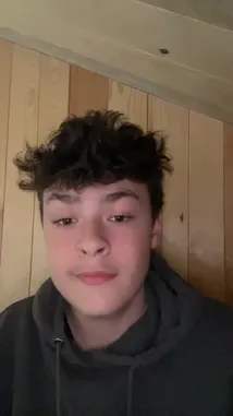 A young man with dark curly hair, wearing a black hoodie, speaks directly to the camera in a room with light-colored wood paneling. He appears to be sharing a personal story or message. In the background, a woman sings a French song. by @justeazure with Original Sound by justeazure