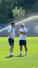 This behind-the-scenes look at Olympique de Marseille's training facility shows the coaching staff actively guiding players during a session. Coaches in team attire are seen giving instructions and observing drills on the pitch, while players wear orange bibs and blue kits. The sunny day and professional setting highlight the intensity of a top-tier football club's preparation. by @omofficial with Original Sound by omofficial