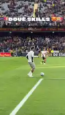In a packed stadium, a soccer player in a white jersey attempts an impressive skill move near the sideline. The crowd watches intently as he juggles the ball, showcasing his talent. The on-screen text 'DOUÉ SKILLS' adds a playful challenge to the moment. by @ligue1 with Original Sound by ligue1