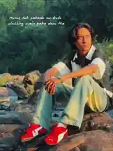A person sits calmly on large rocks beside a flowing river, surrounded by lush greenery. They wear light blue jeans and red sneakers, with their hands resting on their knees. The serene natural setting evokes a sense of tranquility and connection with nature. by @lil.ishhhh with Original Sound by lil.ishhhh