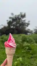 A hand holds a pink soft serve ice cream cone against a lush green background under an overcast sky. The creamy swirl of the ice cream is highlighted as it slightly drips down the cone, capturing a refreshing moment outdoors. This simple, joyful scene evokes feelings of relaxation and summer indulgence. by @nowaira-11 with original sound