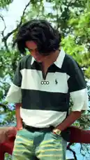 The video opens with a serene shot of a rocky river flowing through a lush forest, accompanied by the hopeful text 'One day we'll explore mountains together it'll be very fun.' It then cuts to a young man with dark, wavy hair, wearing a black and white striped polo shirt and distressed jeans, standing pensively outdoors with his hands in his pockets. The gentle strumming of an acoustic guitar and a soft male vocalist singing in Hindi create a calm, reflective mood, perfectly complementing the scenic beauty and the pensive atmosphere. by @lil.ishhhh with Original Sound by lil.ishhhh