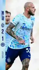 This dynamic video captures an Inter Milan player during a half-time break in a Serie A football match. The athlete, wearing the team's light blue and white patterned jersey with 'betsson' sponsorship and dark blue shorts, showcases his tattoos while moving across the pitch. The scoreboard overlay shows 'HALF TIME' with a score of 2-1 in favor of Inter Milan against Bologna. The player's focused expression and athletic posture highlight the intensity of the game. This moment offers fans a close-up look at one of Inter's key players during a pivotal point in the match. by @interofficial with original sound