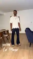 A man, identified as Delly, stands in a modern room at 9:34 PM, showcasing his outfit from 'La Playa'. He wears a distressed white t-shirt, dark flared jeans, and light-colored shoes. The scene is accompanied by a hip-hop track. by @delwinbazilme with Mean It (feat. Ty Dolla $ign) by Nipsey Hussle, Bino Rideaux