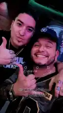 In this intimate selfie-style clip, Tomas Guerrero is seen smiling warmly alongside his cousin in a dimly lit, cozy setting. Both individuals give thumbs-up gestures, showcasing their close bond. The image includes text overlays such as 'Mood' and '@con mi primo @nreal55', emphasizing the familial connection and personal nature of the moment. The atmosphere suggests a casual hangout, possibly at a bar or lounge, with ambient lighting enhancing the relaxed vibe. by @tomasg3901 with original sound