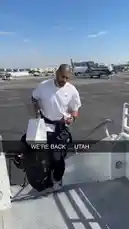 A behind-the-scenes moment shows an LA Clippers player arriving at the airport, carrying his gym bag and coffee. He walks down the aircraft stairs under a clear blue sky, dressed casually in a white t-shirt and navy pants, giving fans a glimpse into the daily routine of a professional athlete. by @clippers with Original Sound by clippers