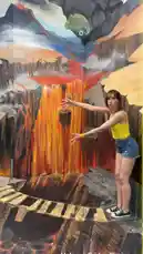 A woman stands on a painted 'bridge' over a fiery volcano, appearing to balance precariously. As she moves her arms, a digital effect makes it look like she's being pulled into the lava below. This 3D illusion art creates a thrilling and interactive experience. by @martine with Original Sound by martine