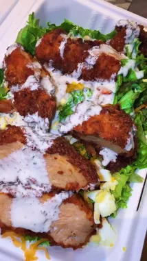 A close-up, mouth-watering view of a perfectly prepared crispy chicken salad served fresh in a takeout container. Juicy, golden-brown breaded chicken pieces rest atop crisp green lettuce, hard-boiled egg slices, and melted cheese, all generously drizzled with creamy ranch dressing. This simple yet satisfying meal highlights delicious textures and flavors, perfect for a quick lunch or dinner. by @riserachelruth with original sound