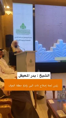 In a formal lecture setting, speaker Yaser Al-Khamsan stands at a podium addressing an audience. A large screen behind him displays his portrait alongside Arabic text, including the phrase 'the foundation of happiness and well-being.' His speech, delivered in Arabic, emphasizes the importance of good character ('الأخلاق الجميلة') as a key component of happiness. by @y_alkhmsan with Original Sound by y_alkhmsan