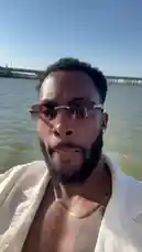 A man, identified as Cole, films himself enjoying a sunny day outdoors. He is seen wearing sunglasses and a white shirt, standing in shallow water with a large bridge visible in the background under a clear blue sky. by @jcoleworld00 with jcoleworld00 by Original Sound