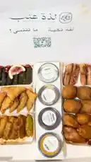 This video offers a mouth-watering close-up tour of a beautifully arranged box of traditional Arabic appetizers from 'Ladha Anab'. The camera pans across a variety of golden-brown fried items, including samosas and kibbeh, alongside vibrant stuffed grape leaves garnished with lemon and pomegranate seeds. The presentation highlights the rich textures and colors of these classic dishes, inviting viewers into a world of authentic Middle Eastern cuisine. by @la_ea10 with Original Sound by la_ea10